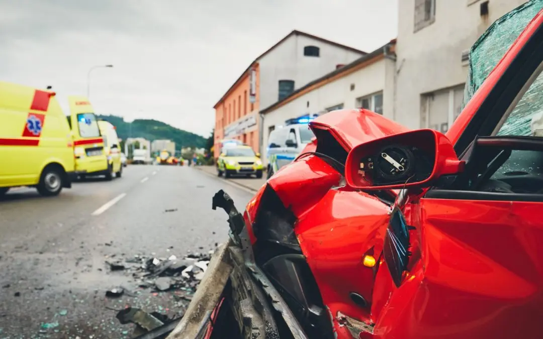Red car crash with emergency vehicles nearby.