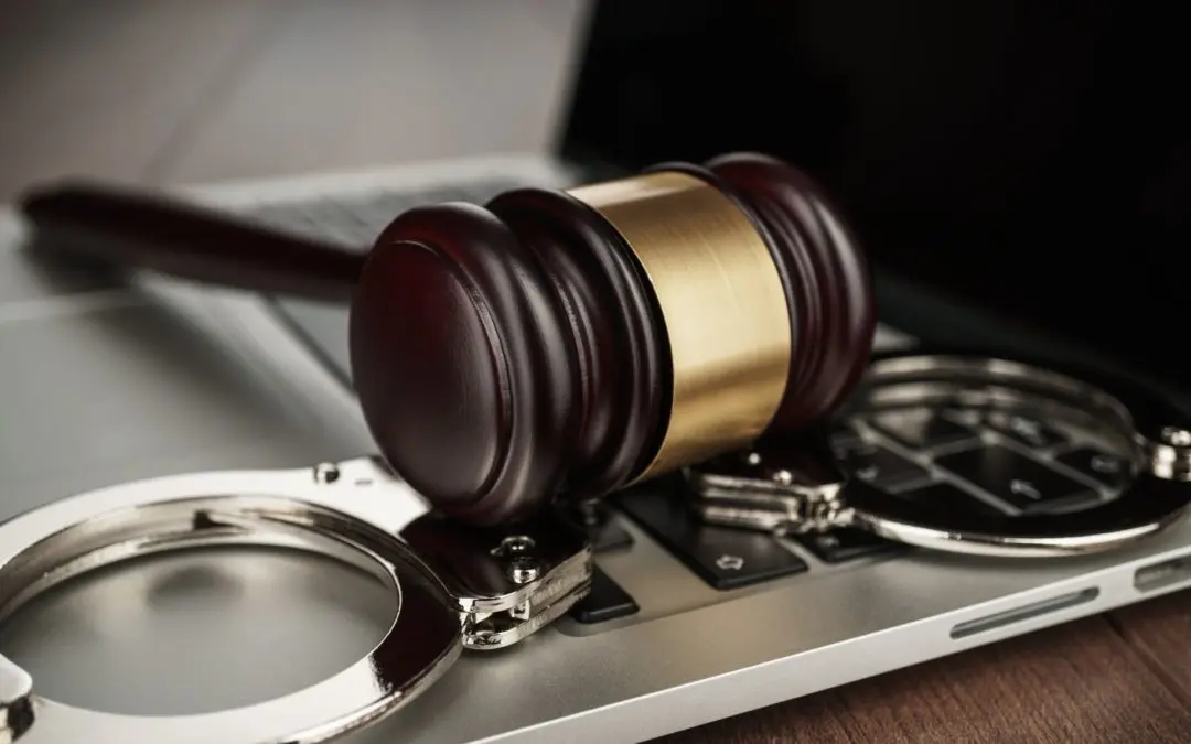 Gavel and handcuffs resting on laptop.
