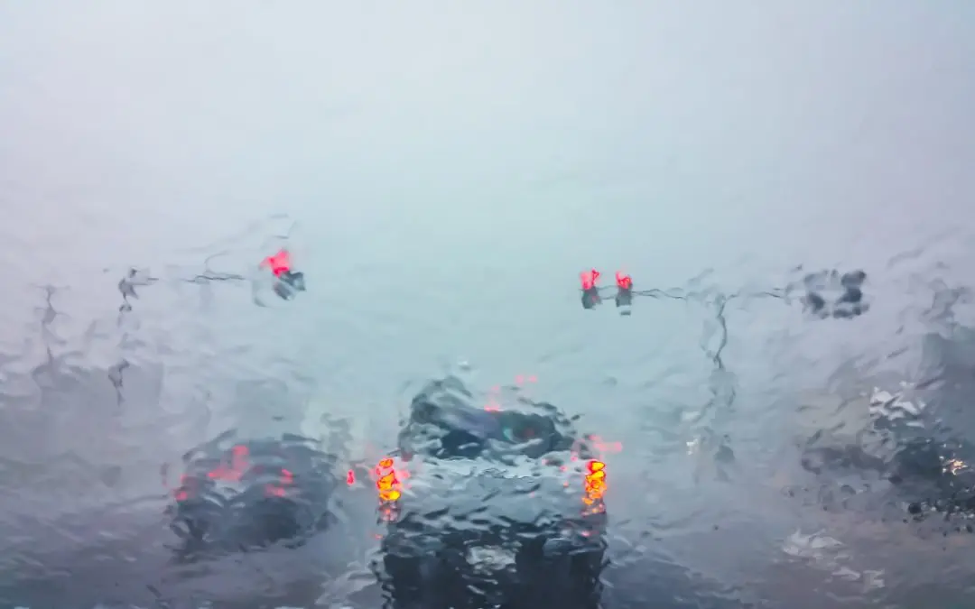 Traffic lights and cars through rainy windshield.