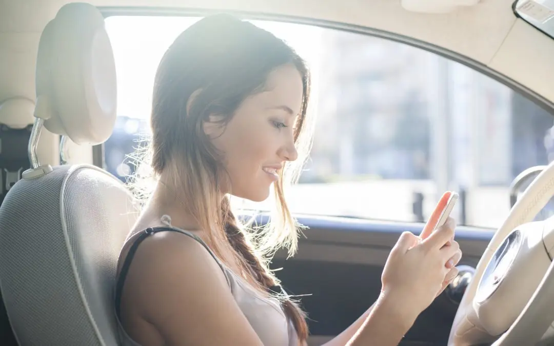 Smiling woman in car using smartphone.