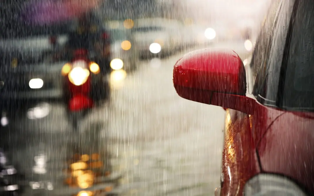 Red car in traffic during heavy rain.