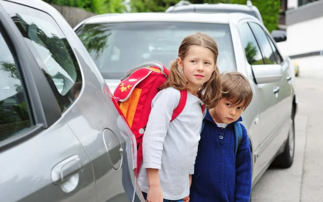 Two children standing beside parked silver car.