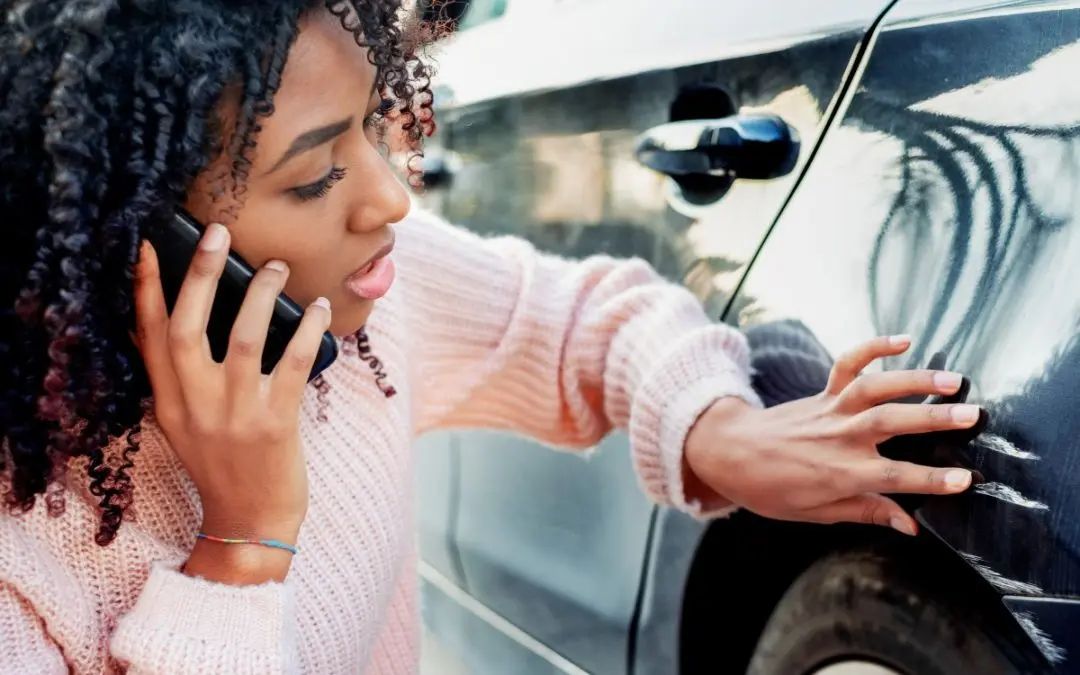 Woman on phone inspecting car's damaged side.
