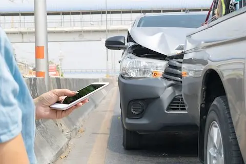 Person holding phone near car accident scene.