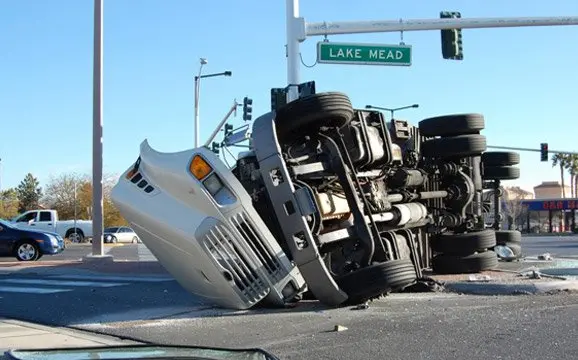 Overturned semi-truck at intersection near sign.