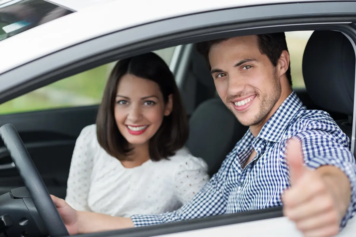 Smiling couple giving thumbs up in car.