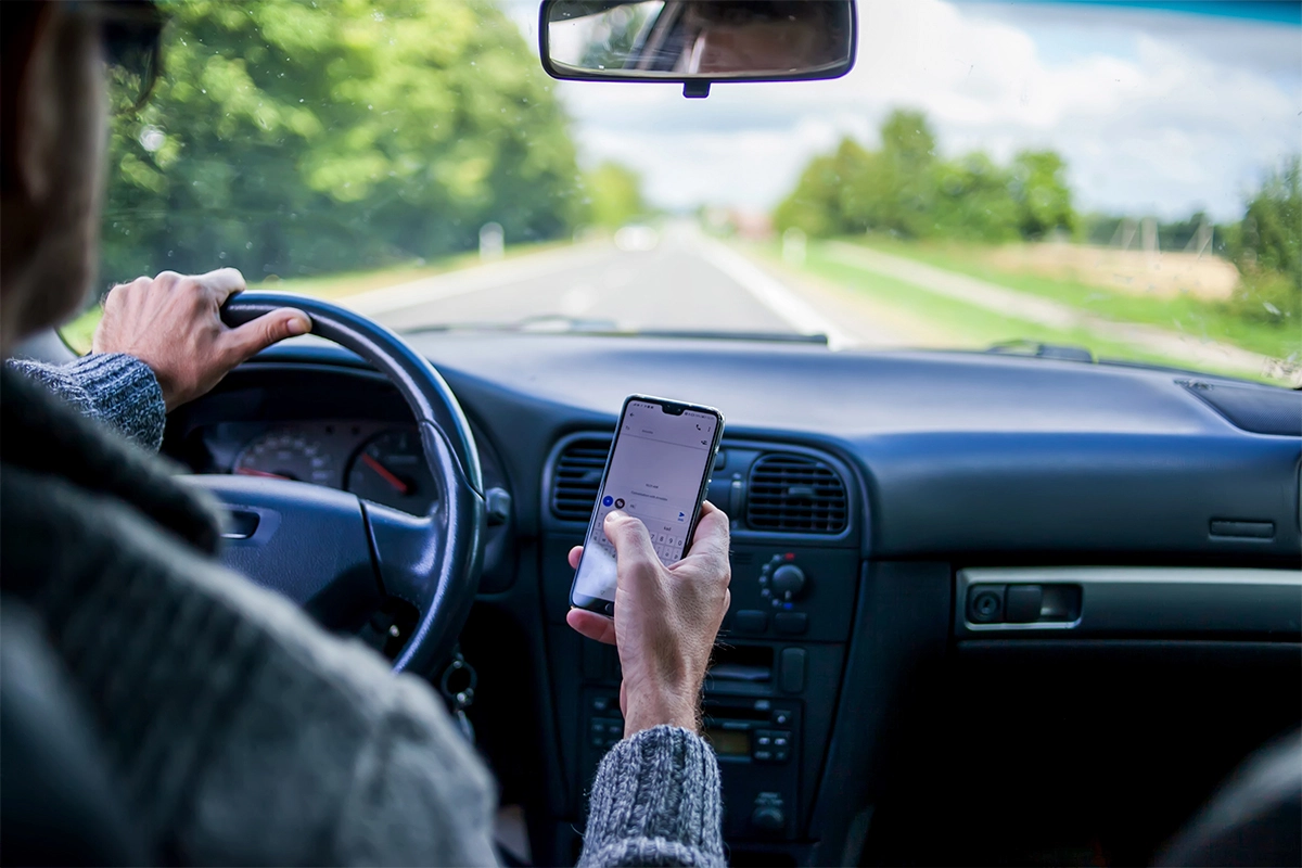 Driver texting on phone while holding steering wheel.