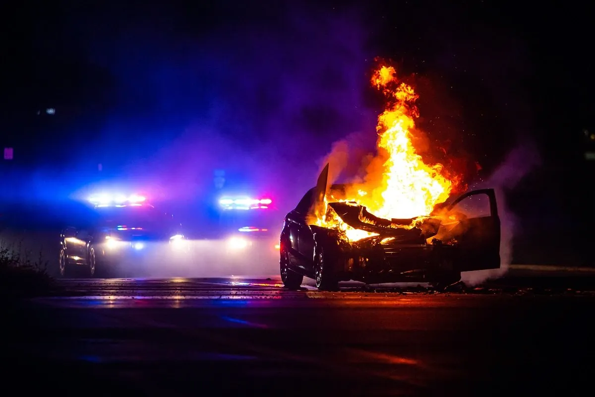 Burning car with police lights behind.