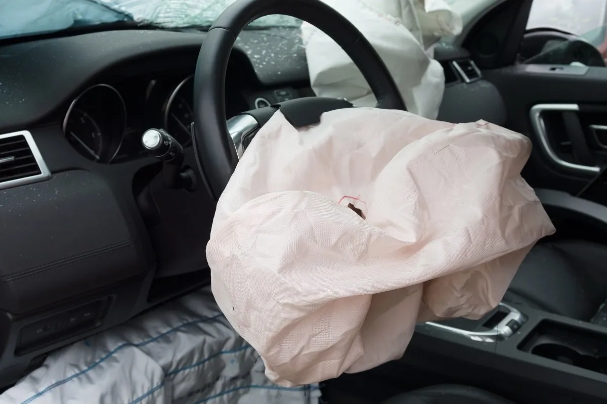 Deployed airbag inside damaged car interior.