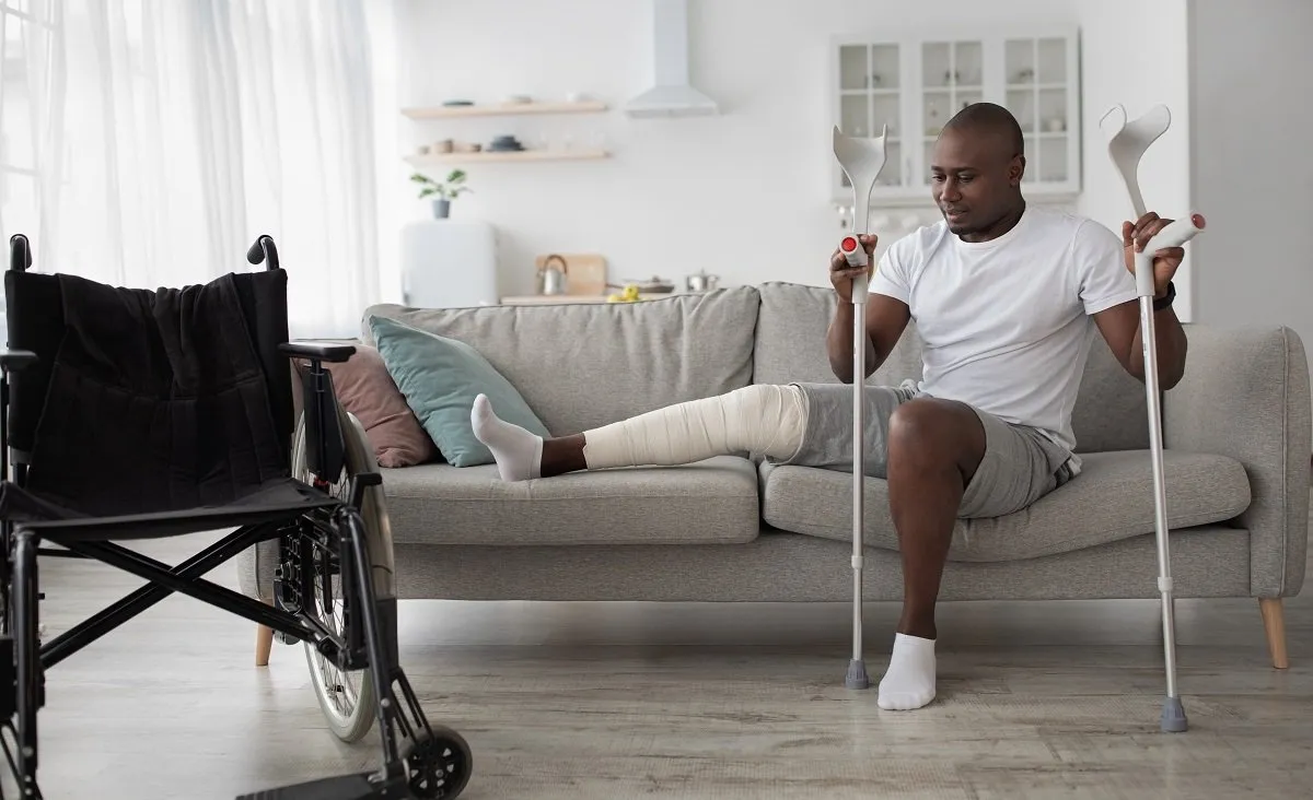 Man with leg cast using crutches indoors.