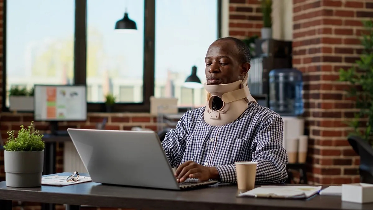 Man wearing neck brace working on laptop.