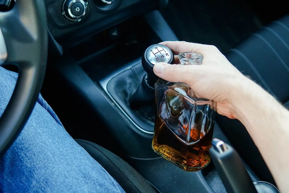 Driver holding liquor bottle while shifting gears.