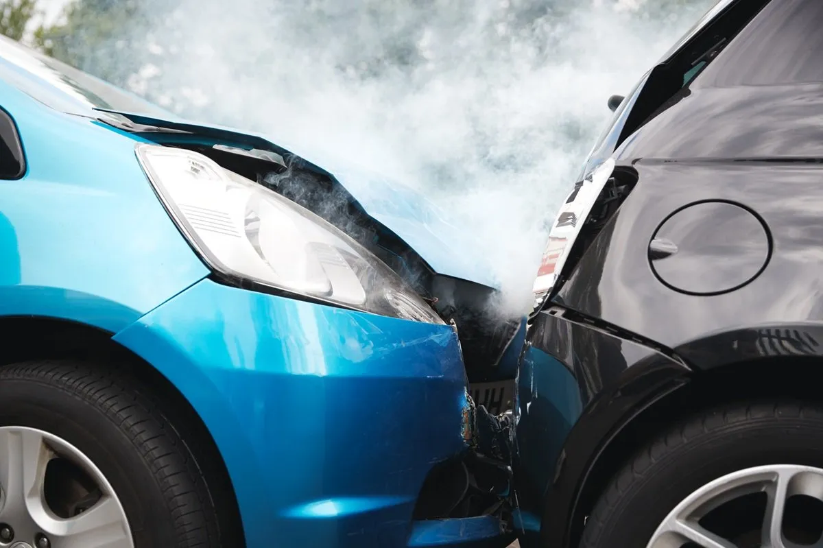 Two cars in a front-end collision smoke.