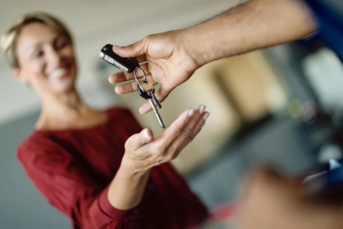 Person handing car keys to smiling woman.