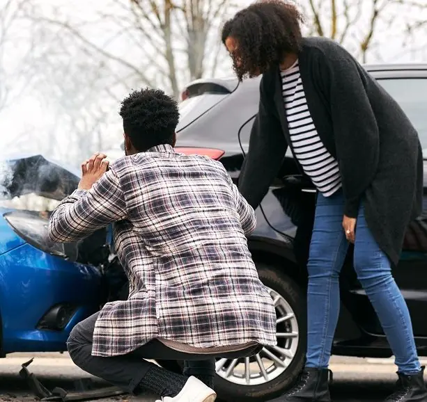 Two people inspecting damage after car crash.