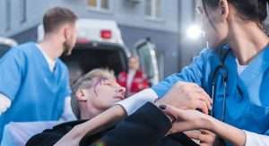 A man on a stretcher is being taken to an ambulance by two nurses.