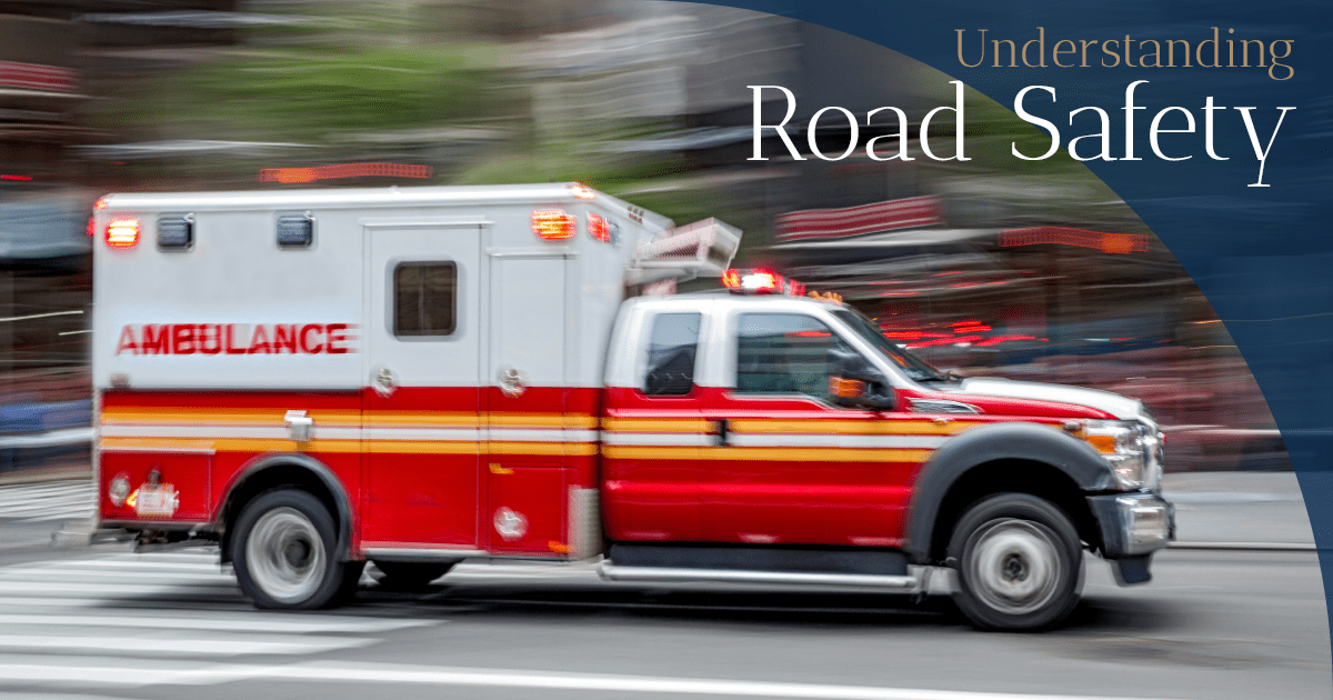 A white and red ambulance with stripes on the bottom half drives on a street.