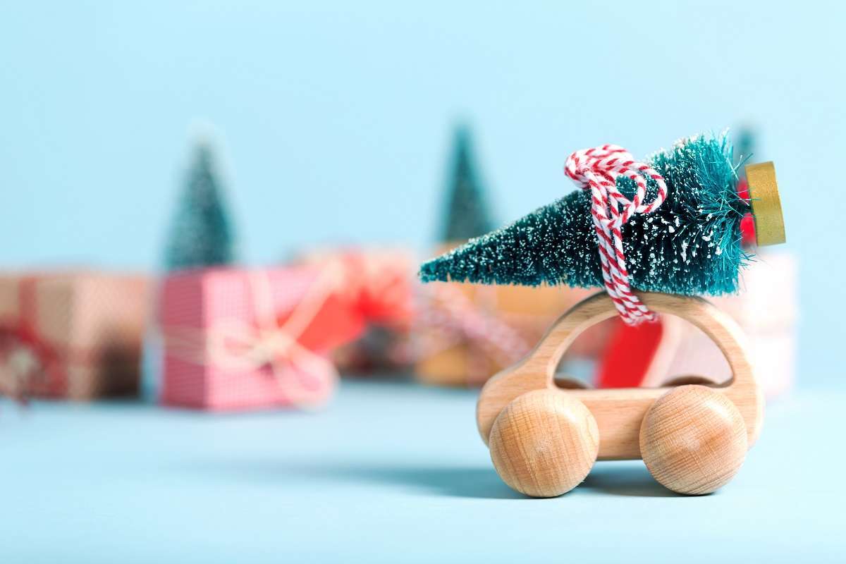 A rounded wooden toy car has a tiny Christmas tree tied to the roof.