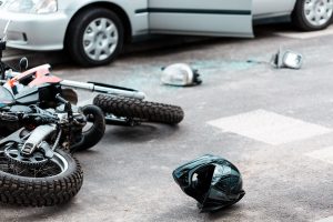 A motorcycle and motorcycle helmet lie close to a car with a broken side mirror nearby.