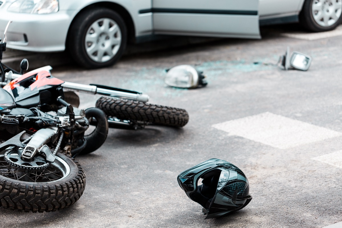 A motorcycle and motorcycle helmet lie close to a car with a broken side mirror nearby.