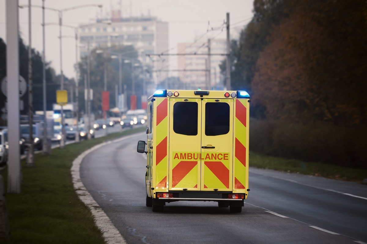 A yellow and red ambulance drives down a road.