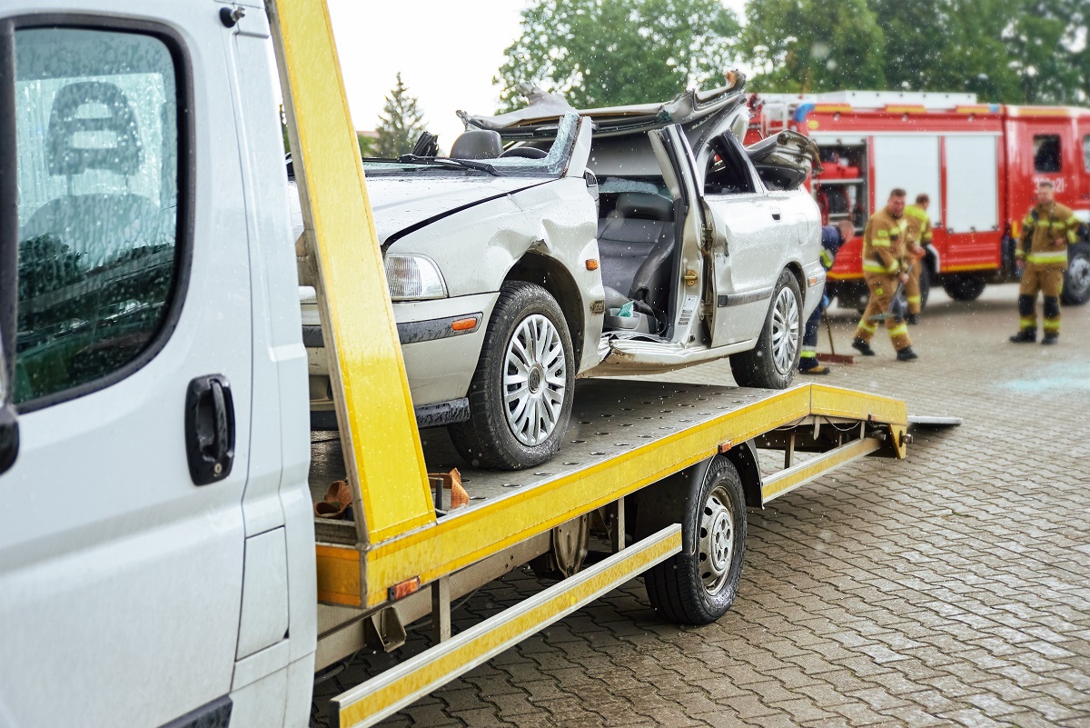 A silver sedan with the roof cut off is on the bed of a large truck.