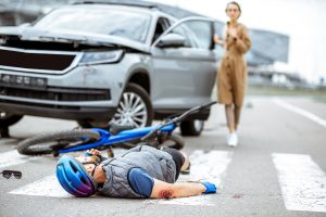 A bicyclist lays on the ground wounded after a collision while the driver exits the vehicle involved.