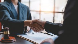 A lawyer shakes hands with her client at a desk with a gavel.