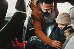 A man buckling a child into a car seat.