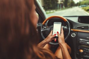 A woman is holding a cell phone with both hands while driving.