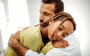 A sad little girl hugs her father.