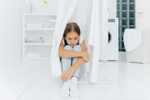 A sad little girl sits alone in a white room