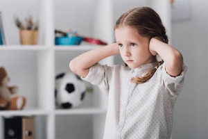 A sad little girl standing with her hands covering her ears